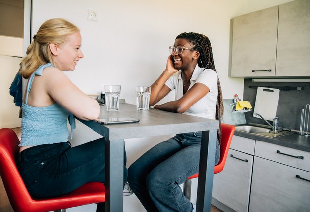 Zwei junge Frauen sitzen an einem Hochtisch in der Küche, lachen und unterhalten sich.