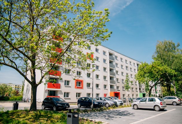 Außenansicht des sechsgeschossigen Studierendenwohnheims in der Makarenkostraße. Vor dem Wohnheim befindet sich ein Parkplatz mit Autos und belaubte Bäume.