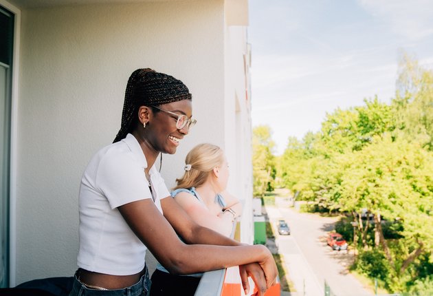Zwei junge Frauen stehen auf einem Balkon des Wohnheims und schauen lachend ins Grüne.